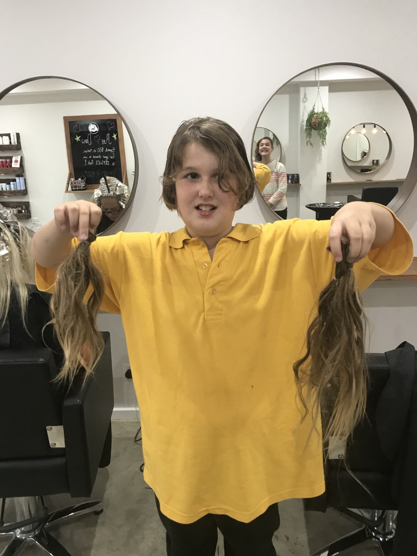 Child proudly holding donated hair after a charity haircut